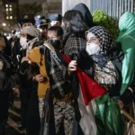 People hold their ground near a main gate at Columbia University in New York, Tuesday, April 30, 2024, as New York City police officers move to clear the area after a building was taken over by protesters earlier today. Colleges and universities have long been protected places for free expression without pressure or punishment. But protests over Israel