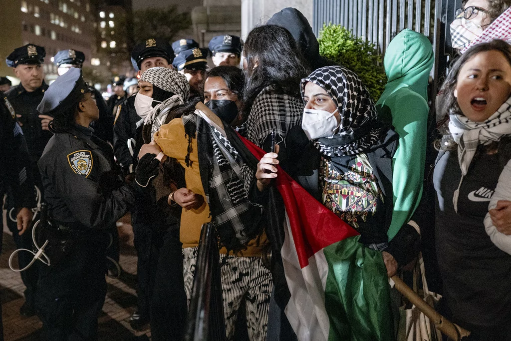 People hold their ground near a main gate at Columbia University in New York, Tuesday, April 30, 2024, as New York City police officers move to clear the area after a building was taken over by protesters earlier today. Colleges and universities have long been protected places for free expression without pressure or punishment. But protests over Israel